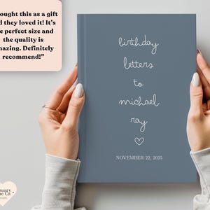 May include: A blue journal with the words "birthday letters to michael ray" in white script. The date "NOVEMBER 22, 2025" is printed at the bottom. The journal is held by a person.