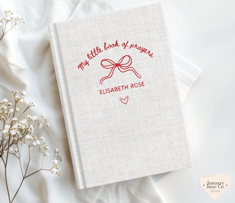 May include: A hardcover book with a light beige linen cover. The title "my little book of prayers" is written in red script, along with the name "ELISABETH ROSE" and a heart icon. The book is a religious item.