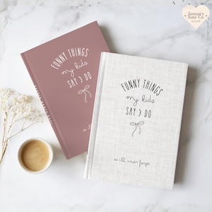May include: Two hardcover journals, one dusty rose and one off-white, with the text "FUNNY THINGS my kids SAY & DO" in black script. Each journal has a bow illustration and the phrase "so I'll never forget." A small cup of coffee sits nearby.