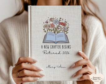 May include: A hardcover journal with a floral design above the text "A New Chapter Begins Retired 2026". The journal cover is light beige with a floral illustration of colorful flowers and an open book.