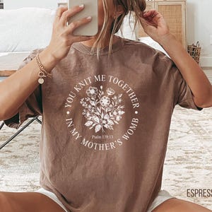 May include: A brown t-shirt with a white floral design and the text "You knit me together in my mother's womb. Psalm 139:13"