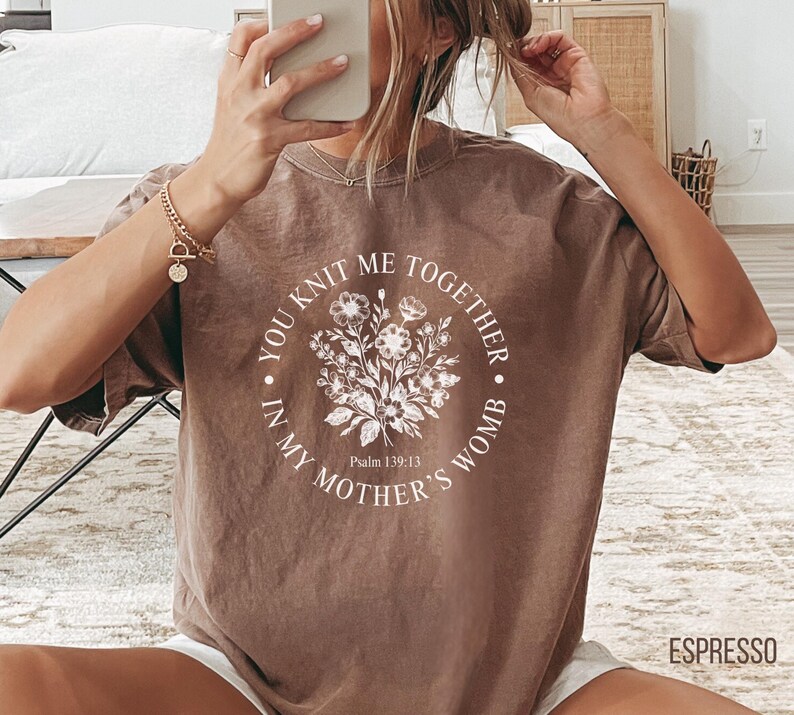 May include: A brown t-shirt with a white floral design and the text "You knit me together in my mother's womb. Psalm 139:13"