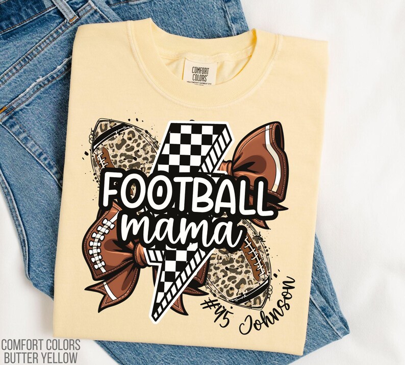 May include: Butter yellow t-shirt with a graphic that says "FOOTBALL mama" in white. The graphic includes footballs, a bow, and a lightning bolt. The shirt also has the text "#45 Johnson".