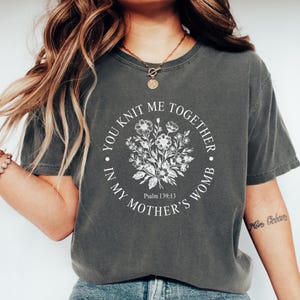 May include: A gray t-shirt with a white graphic that says "You knit me together in my mother's womb" with a floral design and the text "Psalm 139:13".