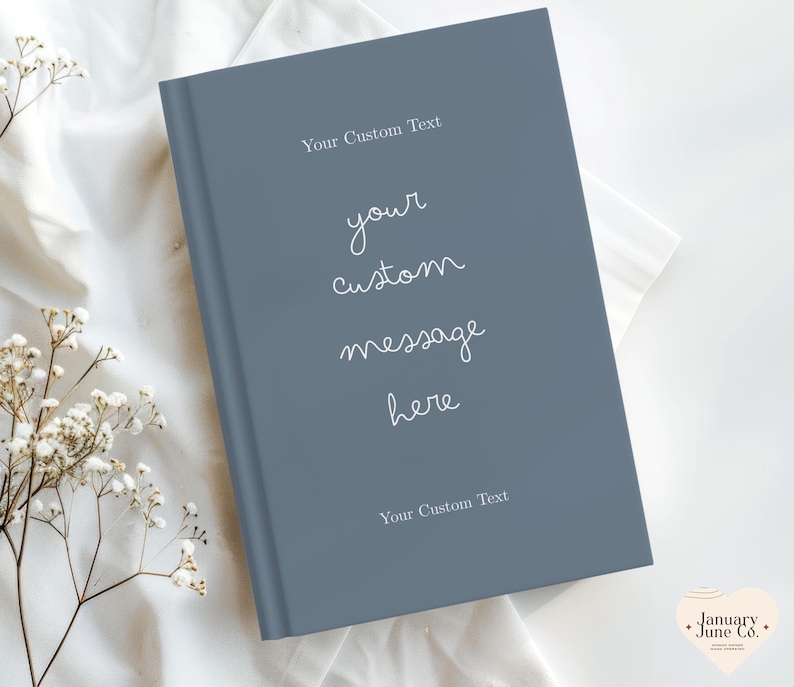 Puede incluir: Un libro de tapa dura con una cubierta azul pizarra. El texto "Your Custom Text" aparece en la parte superior e inferior, con "your custom message here" en el centro. El libro est&aacute; sobre una superficie blanca con detalles florales.