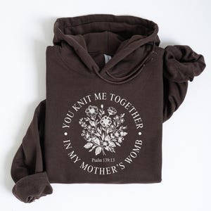 May include: A brown hoodie with a white floral design and the text "You knit me together in my mother's womb" with the scripture reference "Psalm 139:13".