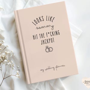 K&ouml;nnte beinhalten: Ein rosafarbenes Hochzeitsplaner-Buch mit schwarzem Text "LOOKS LIKE sammy HIT THE F*CKING JACKPOT". Es enth&auml;lt eine Ringgrafik und die Worte "my wedding planner".