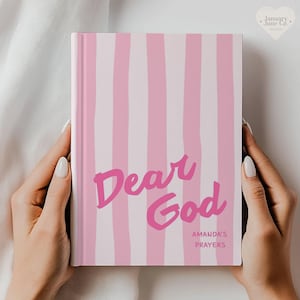 May include: A pink and white striped journal with the words "Dear God" in a handwritten font. The journal also includes the text "Amanda's Prayers". The journal is held by two hands.