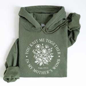 May include: A green hooded sweatshirt with the text "You knit me together in my mother's womb" and a floral design. The text also includes "Psalm 139:13".