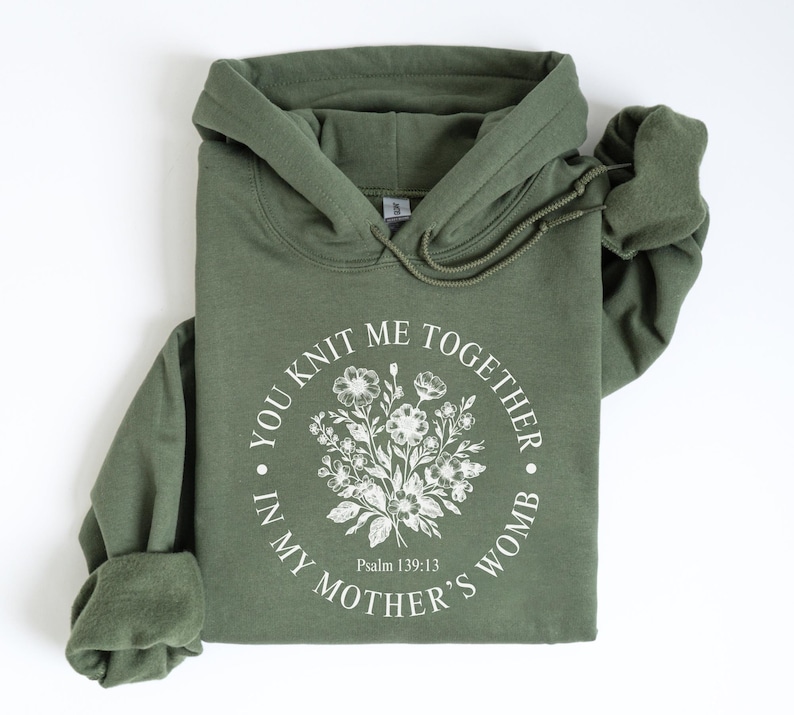 May include: A green hooded sweatshirt with the text "You knit me together in my mother's womb" and a floral design. The text also includes "Psalm 139:13".