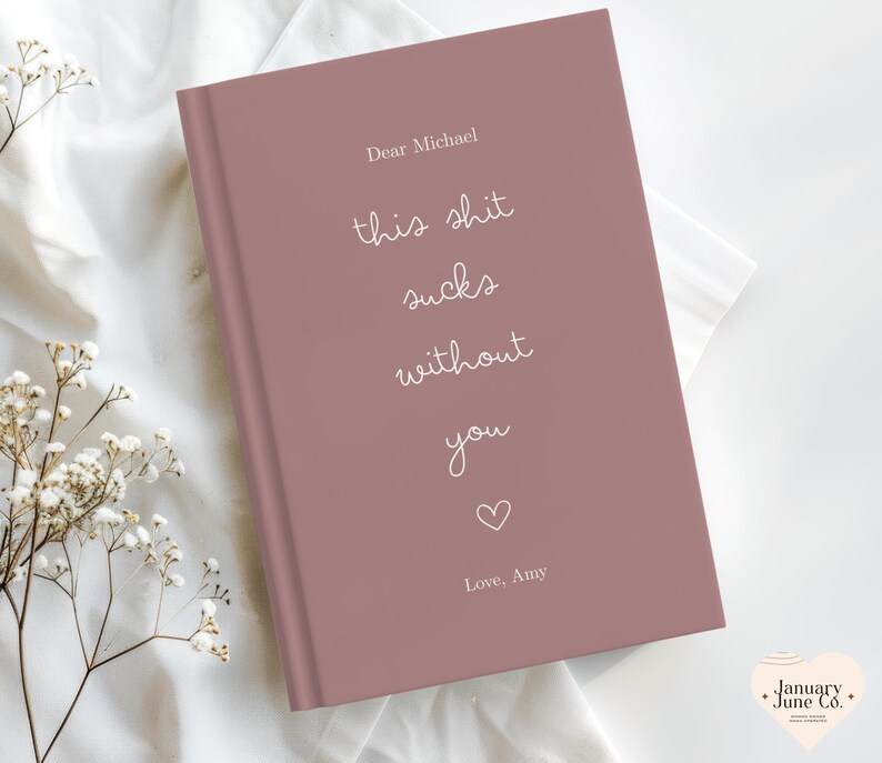Peut inclure: Un journal mauve avec le texte "Dear Michael, this shit sucks without you" en &eacute;criture blanche. Un petit c&oelig;ur et les mots "Love, Amy" sont en dessous. Le journal est sur une surface blanche.