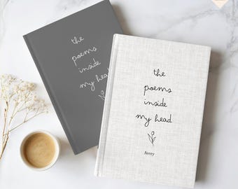 May include: Two hardcover journals with the text "the poems inside my head" in handwritten style. One journal is gray, the other is off-white. A small cup of coffee and a sprig of dried flowers are also in the image.