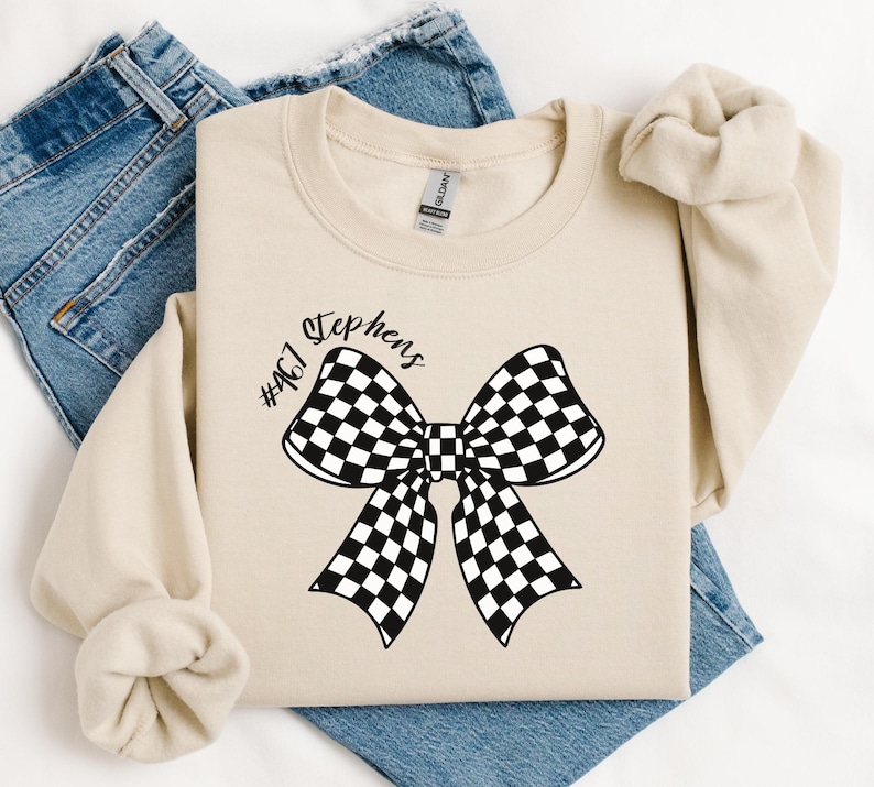 May include: A beige sweatshirt with a black and white checkered bow and the text "#467 Stephens" printed on the front.