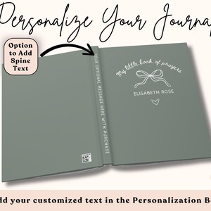 May include: Open journal with a sage green cover, featuring the text "My little book of prayers" and the name "ELISABETH ROSE". A bow and heart are also displayed. The spine reads "YOUR OPTIONAL MESSAGE HERE WITH PURCHASE". The image also includes the text "Personalize Your Journal".