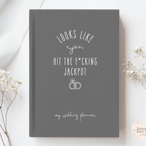 K&ouml;nnte beinhalten: Ein graues Hochzeitsplaner-Notizbuch mit wei&szlig;em Text, der "LOOKS LIKE ryan HIT THE F*CKING JACKPOT" und "my wedding planner" lautet. Das Design beinhaltet zwei Eheringe. Ein Hochzeitsplanungsartikel.