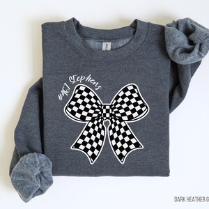 May include: Dark heather grey sweatshirt with a black and white checkered bow and the text "#467 Stephens" printed on the front.