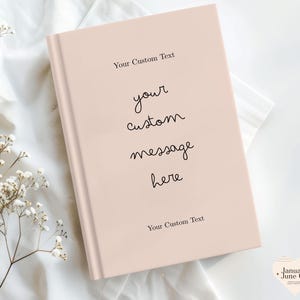 Puede incluir: Un diario de color rosa p&aacute;lido con el texto "Your Custom Text" en la parte superior e inferior. Las palabras "your custom message here" est&aacute;n escritas en cursiva en la portada. El diario est&aacute; sobre una superficie blanca.