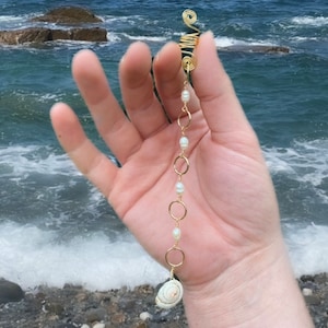 May include: Gold hair coil with a chain of pearls and a seashell charm. The coil is designed to hold hair in place.