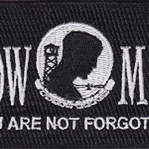 May include: Black and white embroidered patch with the words "POW MIA" and the text "You Are Not Forgotten". The patch features a white silhouette of a prisoner of war with a watchtower in the background.