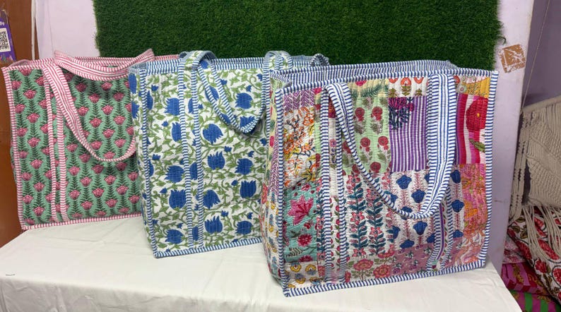 May include: Three tote bags made of patchwork fabric with floral patterns. The bags have blue, pink, green, and white floral designs. The bags have blue and white striped handles.