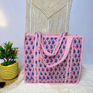 May include: A pink and blue floral tote bag with white stripes. The bag has two long straps and a rectangular shape.