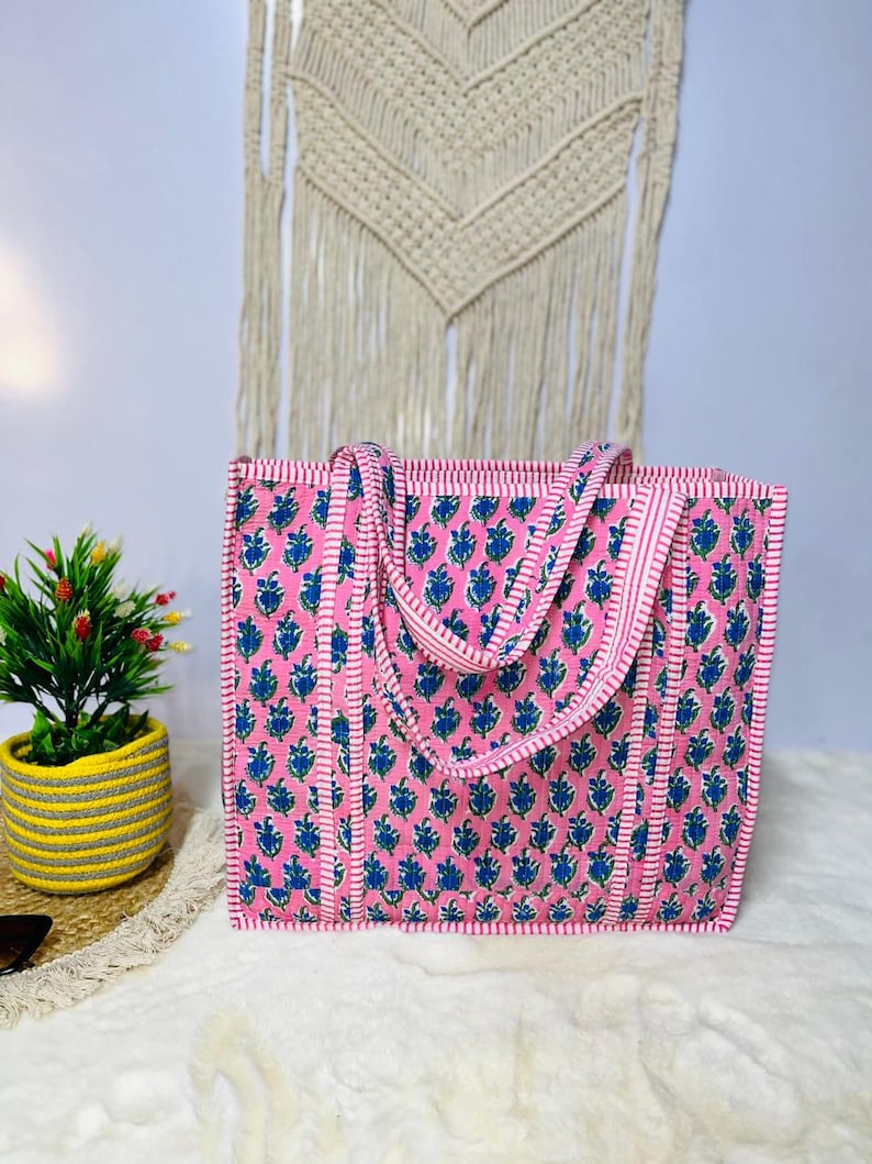 May include: A pink and blue floral tote bag with white stripes. The bag has two long straps and a rectangular shape.
