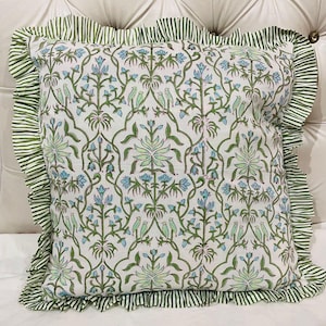 May include: A square throw pillow featuring a white base with a repeating pattern of green vines, light blue flowers, and small green birds. The pillow is finished with a ruffled border made of fabric with thin green and white vertical stripes.