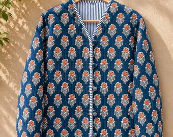 May include: A long-sleeved quilted jacket in deep blue featuring a repeating floral pattern in orange and white. The jacket has a V-neckline, a front button closure with fabric-covered buttons, and blue and white striped trim along the edges.