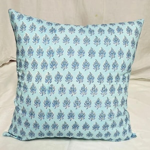 K&ouml;nnte beinhalten: Ein quadratisches Dekokissen mit hellblauem Hintergrund und einem sich wiederholenden Muster aus dunkelblauen Blumenmotiven. Das Design besteht aus kleinen, stilisierten Blatt- und Bl&uuml;tenformen, die in gleichm&auml;&szlig;igen Reihen angeordnet sind.