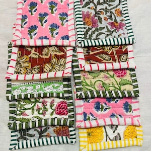May include: A set of ten colorful quilted coasters with floral patterns. The coasters have a variety of colors, including pink, green, yellow, and brown. The coasters are made of fabric and have a quilted design.
