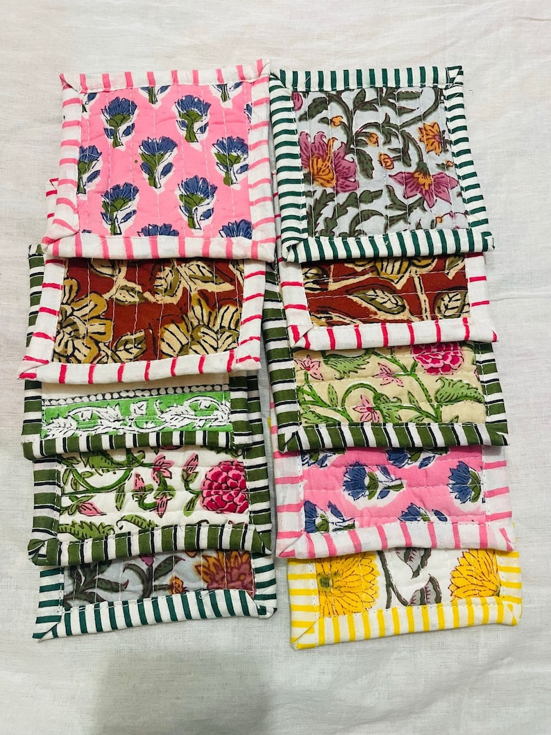 May include: A set of ten colorful quilted coasters with floral patterns. The coasters have a variety of colors, including pink, green, yellow, and brown. The coasters are made of fabric and have a quilted design.
