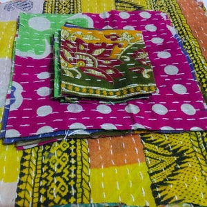 May include: A stack of colorful fabric squares with different patterns, including polka dots, floral designs, and geometric shapes. The fabric is stitched together with white thread.