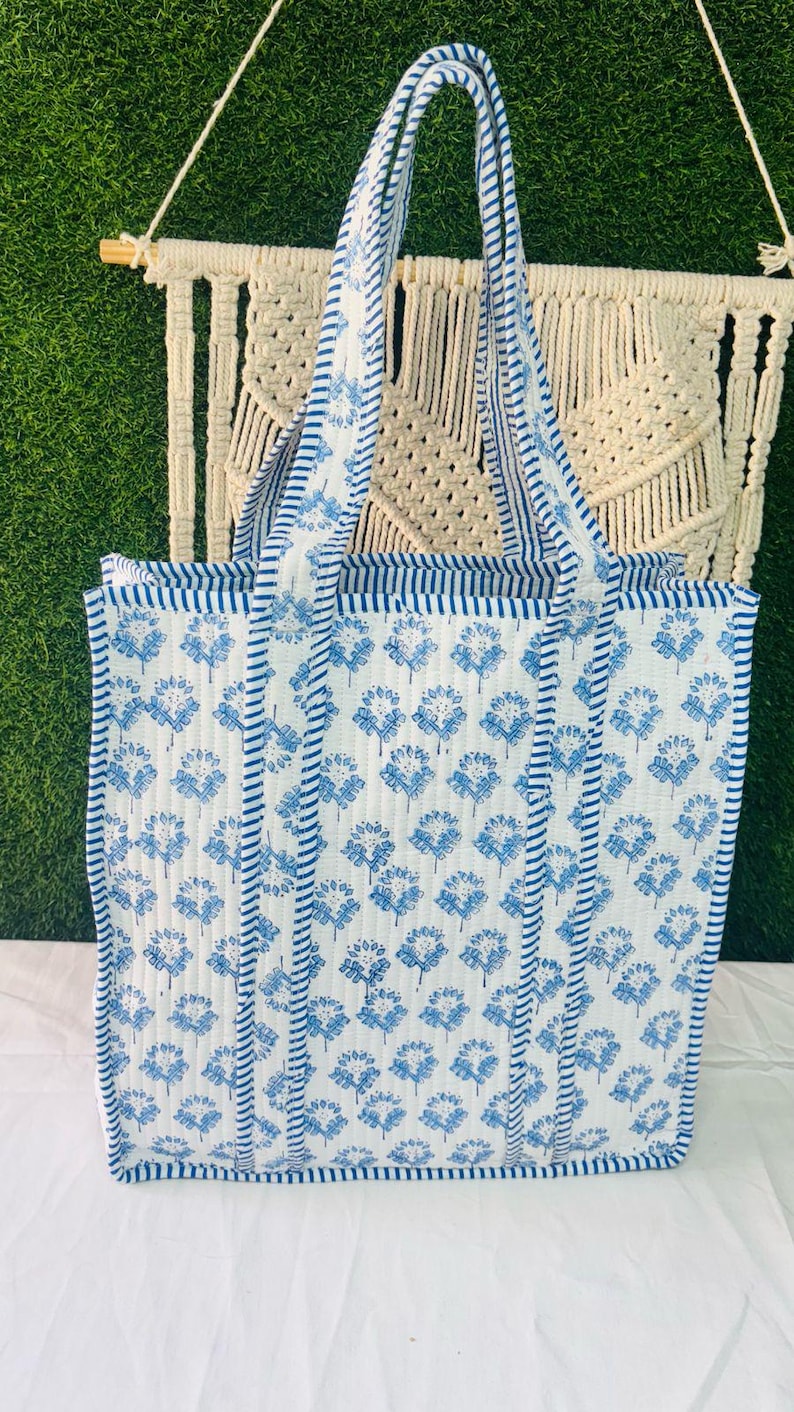 May include: A white tote bag with blue floral print and blue and white striped trim. The bag has two handles.