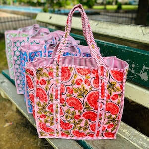 Può includere: Un set di borse tote rosa e bianche con motivi floreali. Le borse hanno manici a righe rosse e bianche e sono realizzate in tessuto intrecciato.