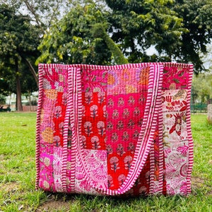 May include: A pink and red patchwork tote bag with white stripes on the straps. The bag is made of quilted fabric and has a floral pattern.