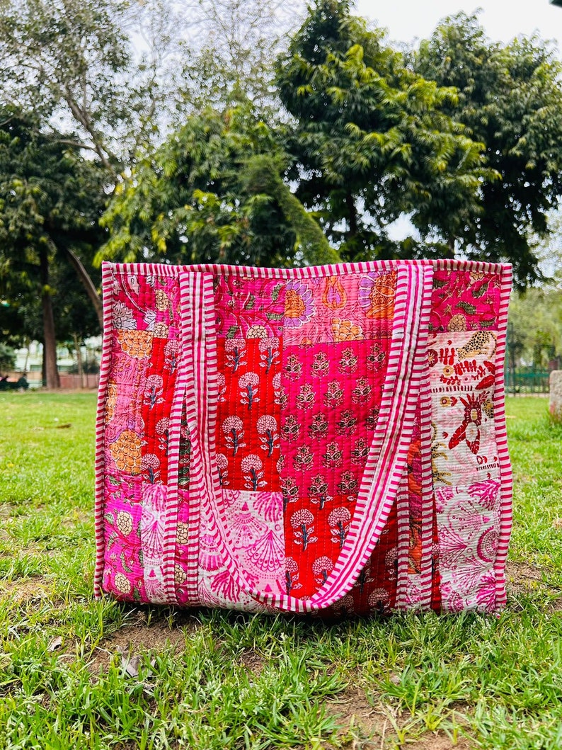 May include: A pink and red patchwork tote bag with white stripes on the straps. The bag is made of quilted fabric and has a floral pattern.