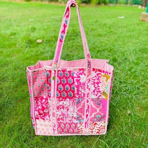 Pu&ograve; includere: Una borsa tote patchwork rosa e bianca con motivi floreali e geometrici. La borsa ha un'unica maniglia ed &egrave; realizzata in tessuto trapuntato.