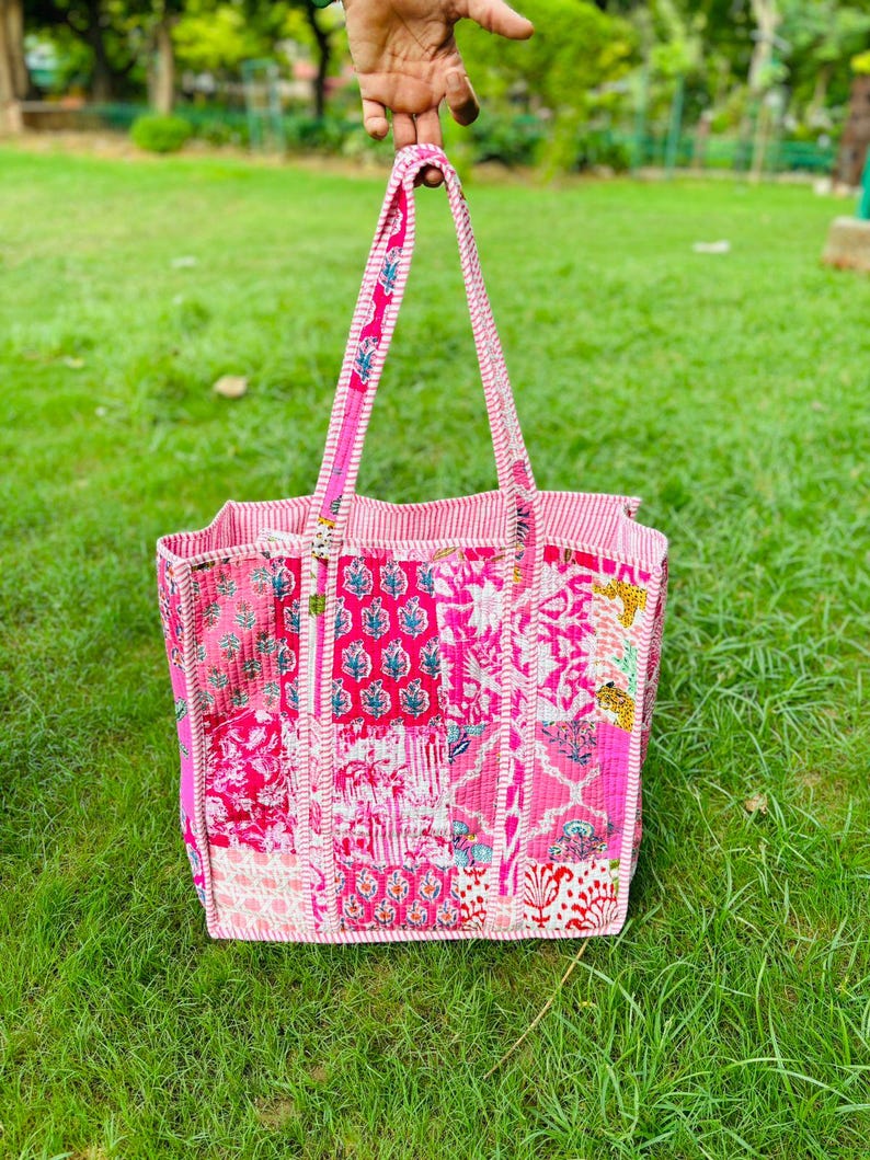 Pu&ograve; includere: Una borsa tote patchwork rosa e bianca con motivi floreali e geometrici. La borsa ha un'unica maniglia ed &egrave; realizzata in tessuto trapuntato.