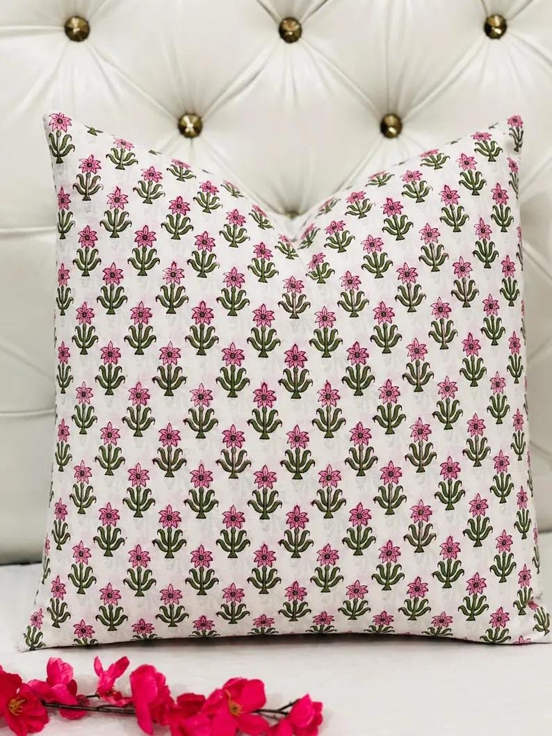 K&ouml;nnte beinhalten: Ein quadratisches Dekokissen mit wei&szlig;em Hintergrund und einem sich wiederholenden Muster aus kleinen rosa Bl&uuml;ten und gr&uuml;nen Stielen. Das florale Design ist in einem gitterartigen Layout &uuml;ber die gesamte Oberfl&auml;che des Kissenbezugs verteilt.