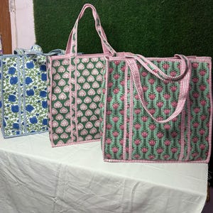 May include: Three tote bags with floral patterns. The bag on the left is blue and white, the middle bag is green and white, and the bag on the right is green and pink.