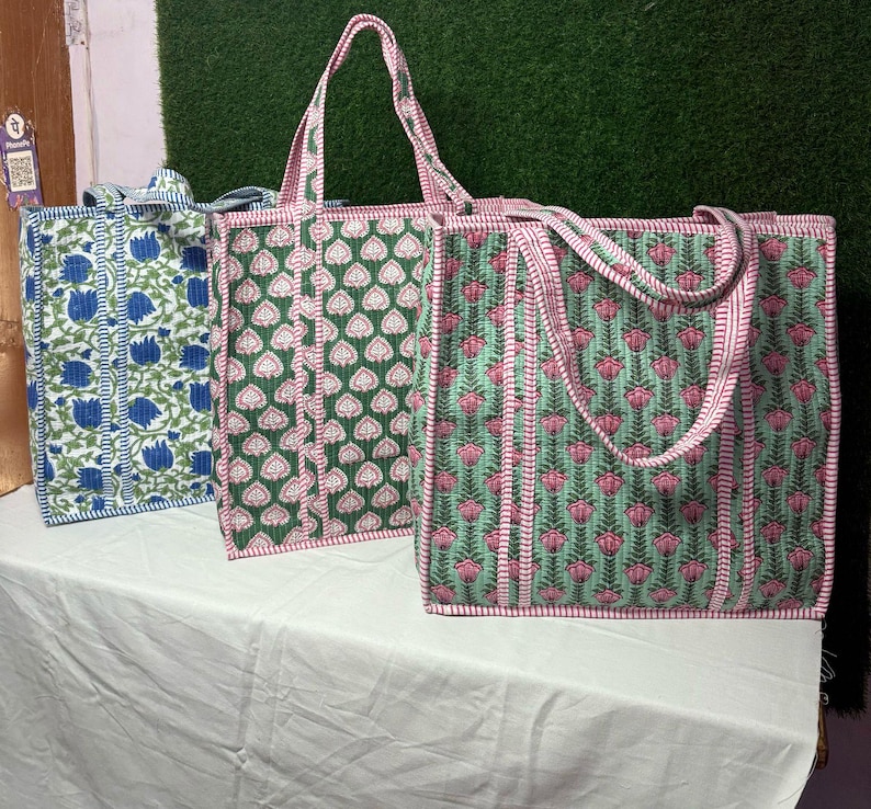 May include: Three tote bags with floral patterns. The bag on the left is blue and white, the middle bag is green and white, and the bag on the right is green and pink.