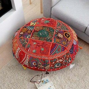 May include: A round, red, multi-colored, patchwork floor cushion with intricate embroidery and tassels. The cushion is made of various fabrics and features a floral design.