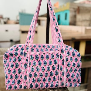 May include: Pink and blue floral patterned tote bag with matching handles. The bag features a rectangular shape with a zipper closure and a white stripe detail. The bag is made of a soft fabric.