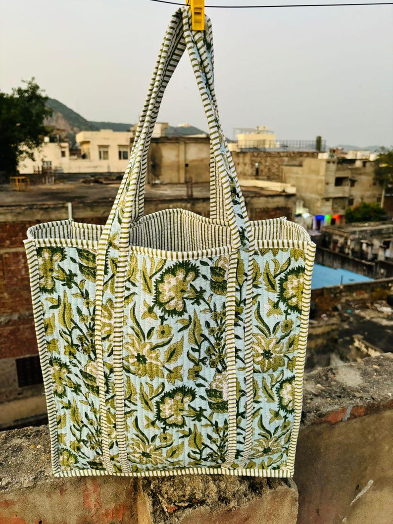 May include: A green and white floral tote bag with striped handles. The bag is made of quilted fabric and has a light blue background.