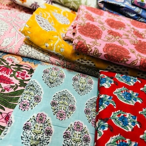 Puede incluir: Una pila de telas coloridas con patrones florales. Las telas son en tonos de rosa, rojo, azul, amarillo y verde. Los patrones son intrincados y detallados.