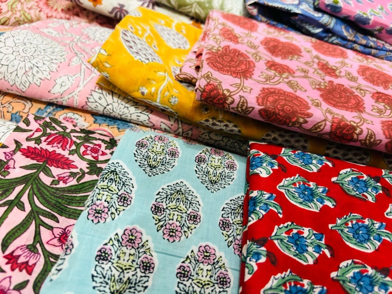 Puede incluir: Una pila de telas coloridas con patrones florales. Las telas son en tonos de rosa, rojo, azul, amarillo y verde. Los patrones son intrincados y detallados.