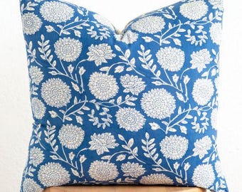 May include: A square decorative pillow with a blue background and a white floral pattern. The pillow is placed on a small wooden stool. The floral design includes large flowers and leafy vines.