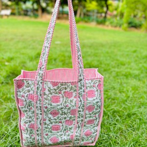 Pu&ograve; includere: Una borsa tote rosa e bianca con stampa floreale. La borsa ha manici a righe rosa e bianche.