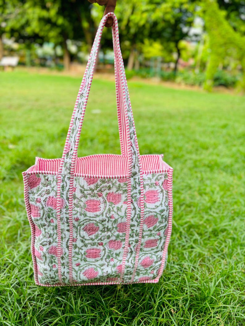 Pu&ograve; includere: Una borsa tote rosa e bianca con stampa floreale. La borsa ha manici a righe rosa e bianche.