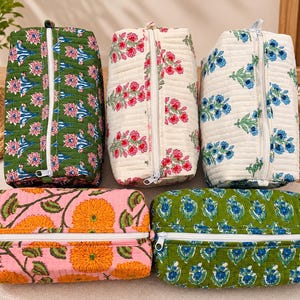 May include: Five rectangular quilted pouches with white zips. One is green with pink floral patterns, one is cream with pink flowers, one is cream with blue flowers, one is pink with orange flowers, and one is green with blue floral motifs.